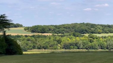 Yumuşak mavi gökyüzünün altındaki katmanlı İngiliz kırsal tepelerinin ve ağaçların geniş bir görüntüsü, yaz ışığı altında, yavaş çekimde.