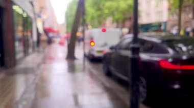 Yağmurlu bir Londra caddesinin bulanık görüntüsü, şemsiyeler, kırmızı çift katlı otobüsler, ve damlayan ağaçların altından geçen yayalar, atmosferik ve dengesiz, dağılmış