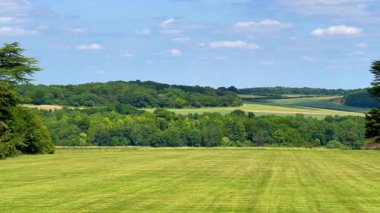 Yumuşak mavi gökyüzünün altındaki katmanlı İngiliz kırsal tepelerinin ve ağaçların geniş bir görüntüsü, yaz ışığı altında, yavaş çekimde.