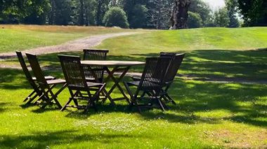 Ahşap bahçe masası ve İngiliz kırsal kesimindeki ağaçların altındaki çimenlerin üzerinde sandalyeler, yavaş çekim.