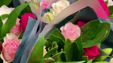 Çiçekçide sergilenen çiçekler, yumuşak kağıt buketlerde toplanmış taze yeşillik ve hassas tonlarda, yavaş çekim