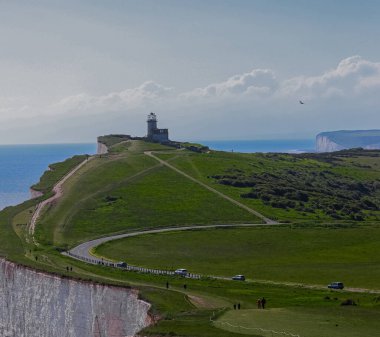 Clifftop road and walking path lead to coastal lighthouse above chalk cliffs and shoreline in East Sussex, concept of navigation, heritage trail and scenic coastal route in the English seaside countryside