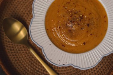 Warm pumpkin soup in a bowl topped with chili flakes, ready to eat, served on a woven mat. Comforting autumn food concept