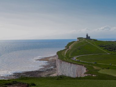 Beachy Head lighthouse standing on white chalk cliff by the sea, attracting tourists. East Sussex countryside, England