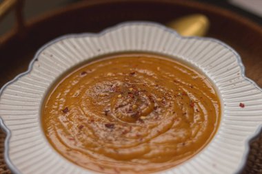 Beyaz deniztarağı kenarlı kasede servis edilen portakallı kremalı çorba. Baharatlı bir dokunuş için kırmızı biber taneleriyle süslenmiş.