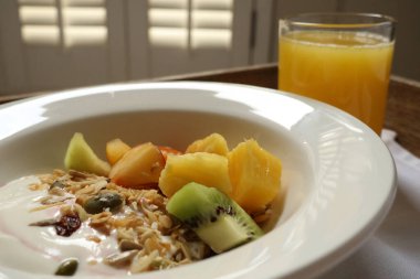 Sağlıklı yoğurt, tahıl gevreği ve portakal suyu ile dilimlenmiş meyve içeren kahvaltı kasesi. Cotswold kırsal, İngiltere