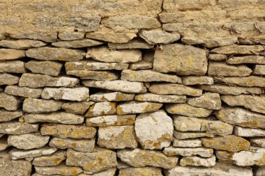 Stone wall presenting a rustic texture with natural rock formations. Ancient building material creating an aged and weathered background. Cotswolds, England