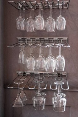 Clear crystal wine glasses, cocktail glasses, and martini glasses hanging on metal bar racks, clean and organized