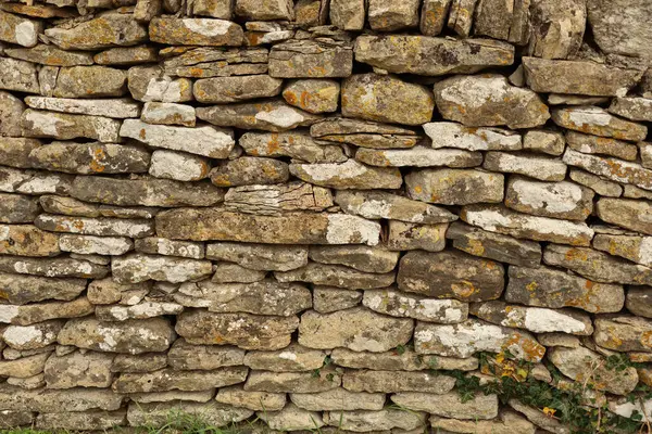 Düzensiz kayalarla kaplı kuru taş duvar yapısı doğal bir doku, arka plan ve yaşlanmış bir yüzey yaratıyor. Cotswolds, İngiltere