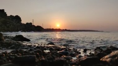 Bu video, deniz taşları üzerinde güneşin doğuşunun nefes kesici güzelliğini yakalar. Güneş ufuktan yavaşça yükselirken deniz kayaları üzerinde sıcak ve altın renkli bir parıltı saçarak büyüleyici ve huzurlu bir manzara yaratıyor..