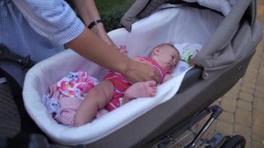 Yakın plan. Annem bebeği kollarına alır. Bir kadın bebek arabasından bir çocuk çıkarır ve onu kendi üzerine kaldırır. 4K Ağır çekim