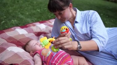 Annem parkta bebekle oynuyor. Kadın bir kıza parlak bir oyuncak gösterir. 4K Ağır çekim