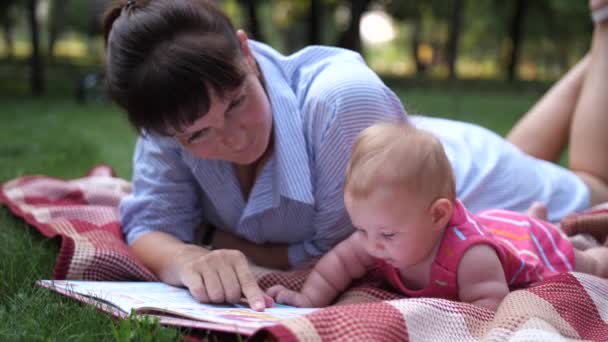 妈妈和女儿躺在公园的肚子上 妈妈给女婴看明亮的书 4K慢速Mo — 图库视频影像
