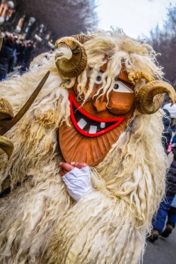 A vibrant character in a fluffy, horned costume takes center stage during a winter street festival. The joyful mask features a big smile, adding to the festive atmosphere of the event. clipart