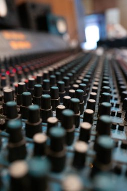 This shot features a detailed view of an audio mixing console, showcasing multiple knobs and faders set within a recording studio, creating a professional atmosphere for music production. clipart