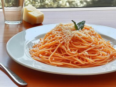 A fork twirls a generous portion of spaghetti topped with cheese and a fresh basil leaf, set against a warm wooden table. Nearby, a glass of water and a piece of cheese rest. clipart