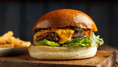 A delicious smash burger features a perfectly seared beef patty with crispy edges. Topped with melted cheese, fresh lettuce, and pickles, this appetizing meal is served alongside golden fries on a rustic wooden surface. clipart