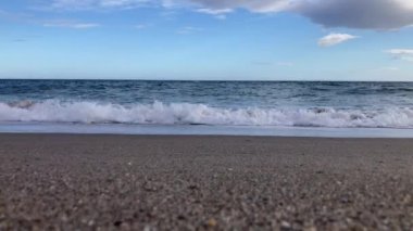 Akdeniz 'in videosu. Dalgalar bulutlu bir gökyüzüne karşı kumlu bir kıyıya çarpar.