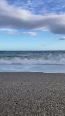 Akdeniz 'in videosu. Dalgalar bulutlu bir gökyüzüne karşı kumlu bir kıyıya çarpar.