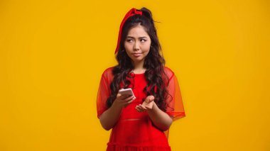 Kırmızı elbiseli kafası karışık Asyalı kadın sarı telefonda mesaj atıyor. 