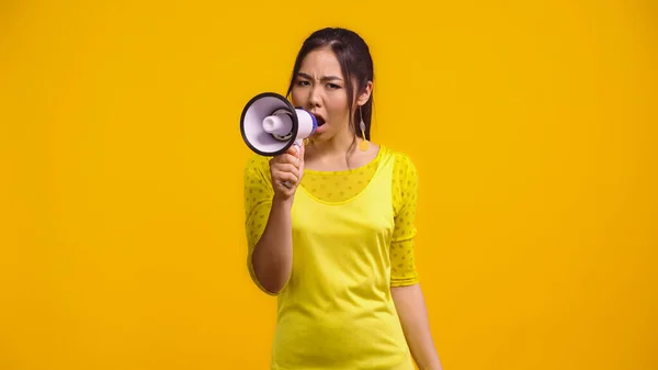 stock image displeased asian woman screaming in megaphone isolated on yellow 