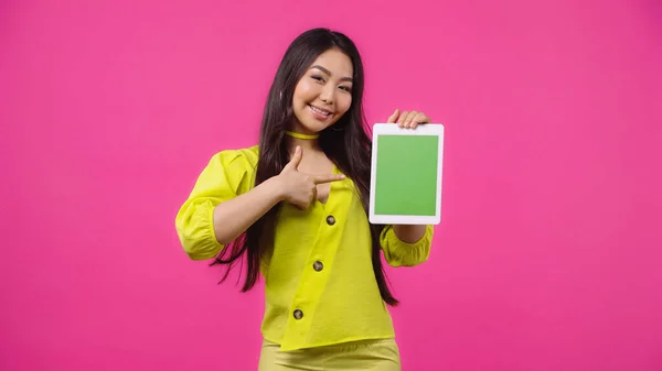 快乐的亚洲女人指着数字平板电脑 绿色屏幕与粉色隔离 — 图库照片