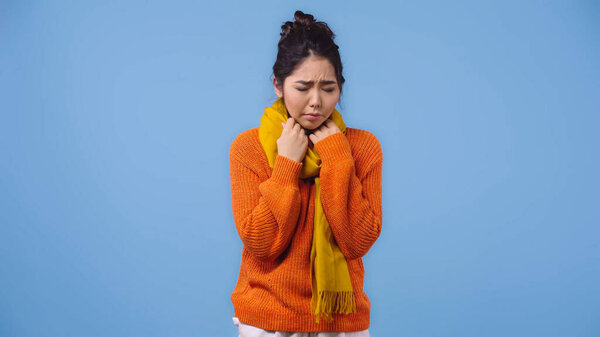 sick asian woman in orange sweater and scarf feeling unwell isolated on blue 