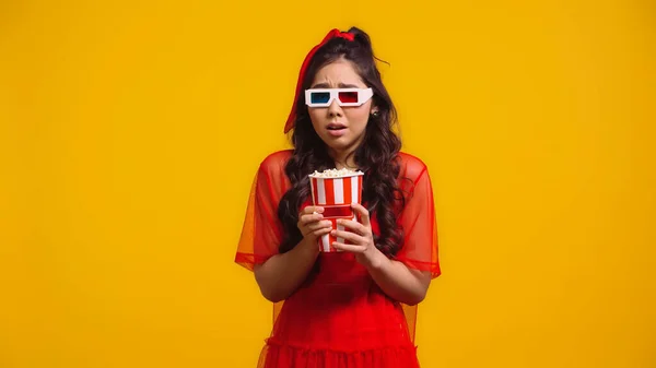 Scared asian woman in 3d glasses eating popcorn isolated on yellow — Stock Photo