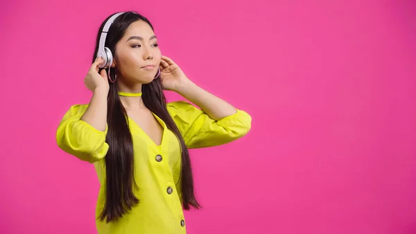 Giovane donna asiatica in cuffie wireless ascoltare musica isolata su rosa — Foto stock