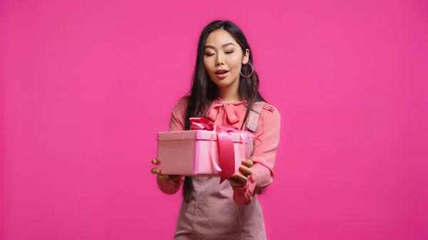 Здивована молода азіатська жінка тримає загорнутий подарунок ізольовано на рожевому — стокове фото