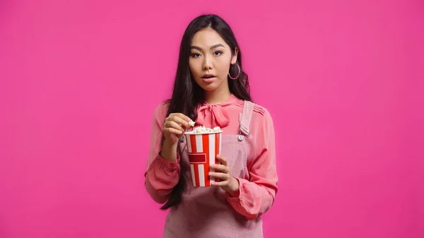 Bastante joven asiático mujer con abierto boca celebración palomitas de maíz cubo aislado en rosa — Stock Photo