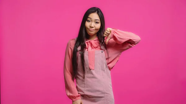 Displeased and young asian woman looking at camera while showing thumb down isolated on pink — Stock Photo