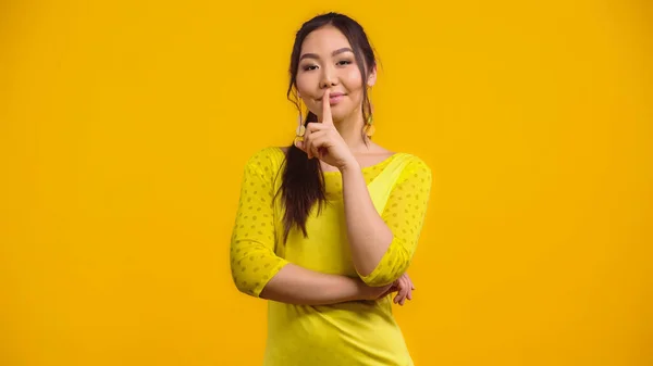 Happy asian woman showing hush sign and smiling isolated on yellow — Stock Photo
