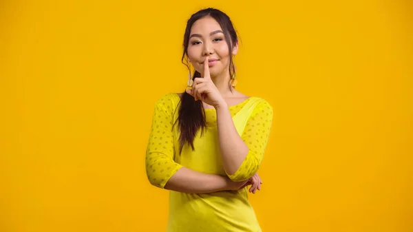 Felice donna asiatica mostrando segno di silenzio e sorridente isolato su giallo — Foto stock
