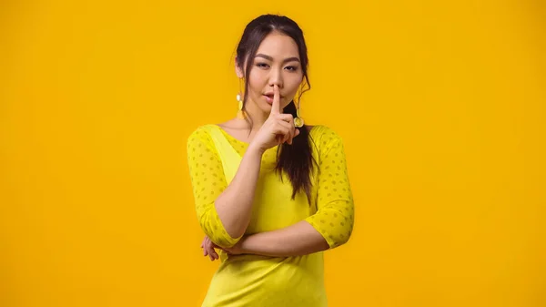 Young asian woman showing hush sign and smiling isolated on yellow — Stock Photo