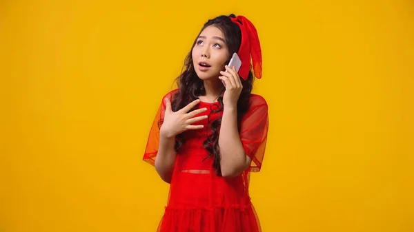 Emocional asiático mulher no vermelho vestido falando no smartphone isolado no amarelo — Fotografia de Stock