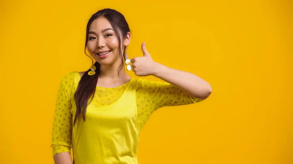 Feliz asiático mujer mostrando pulgar arriba y sonriendo aislado en amarillo - foto de stock