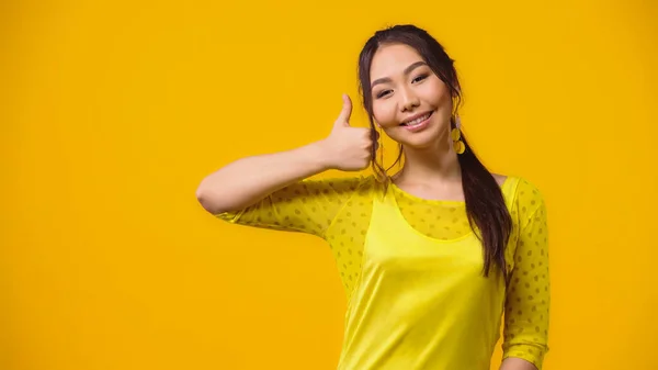 Positive asiatische junge Frau zeigt Daumen nach oben isoliert auf gelb — Stockfoto