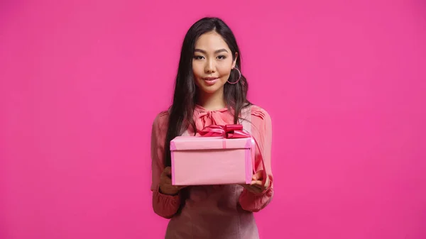 Веселая молодая азиатская женщина держит завернутый подарок изолирован на розовый — стоковое фото