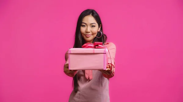 Complacido joven asiático mujer holding envuelto presente aislado en rosa - foto de stock