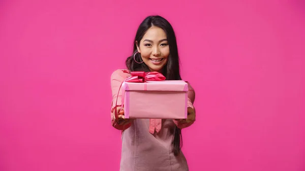 Glücklich junge asiatische Frau gibt verpacktes Geschenk isoliert auf rosa — Stockfoto