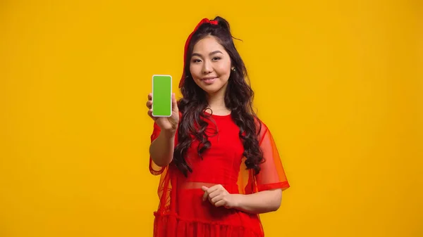 Heureux asiatique femme tenant smartphone avec écran vert isolé sur jaune — Photo de stock