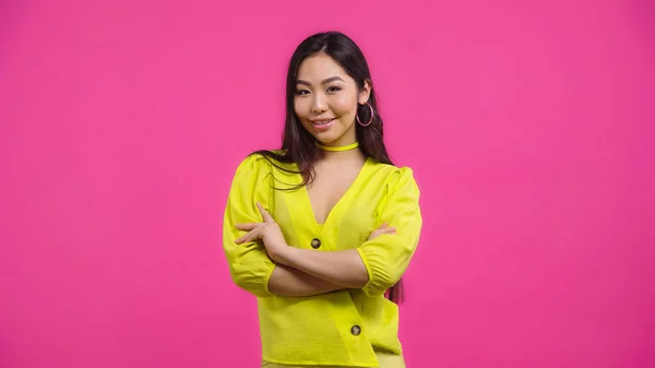 Bonita mujer asiática de pie con brazos cruzados aislados en rosa — Stock Photo