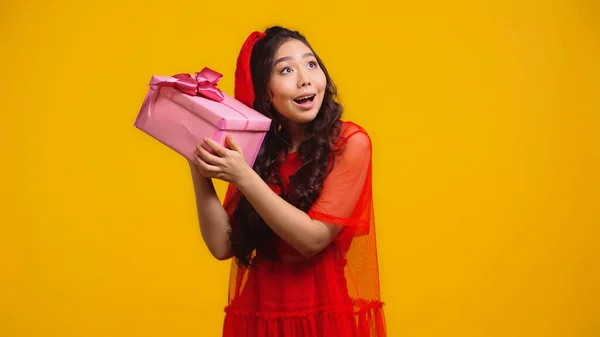 Цікава азіатська жінка тримає загорнутий подарунок ізольовано на жовтому — стокове фото