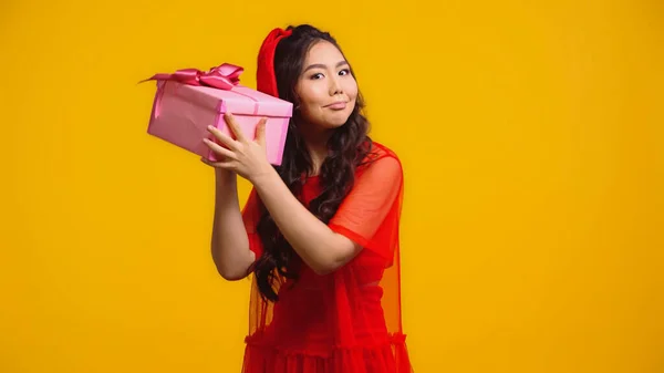 Uncertain young asian woman shaking wrapped present isolated on yellow — Stock Photo