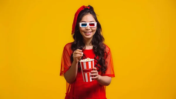Glücklich asiatische Frau in 3D-Brille halten Popcorn und sehen Film isoliert auf gelb — Stockfoto