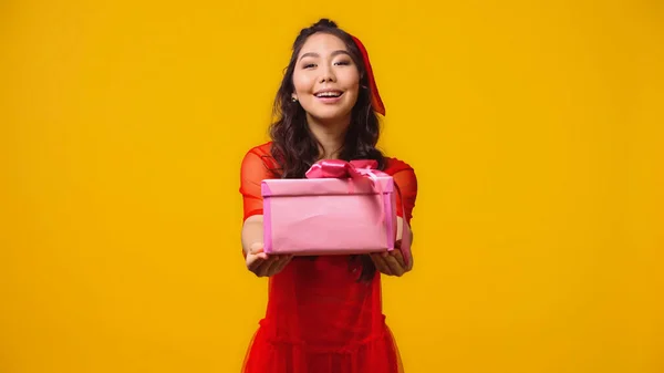 Положительный и молодой азиатской женщины, давая завернутый подарок изолированы на желтый — стоковое фото