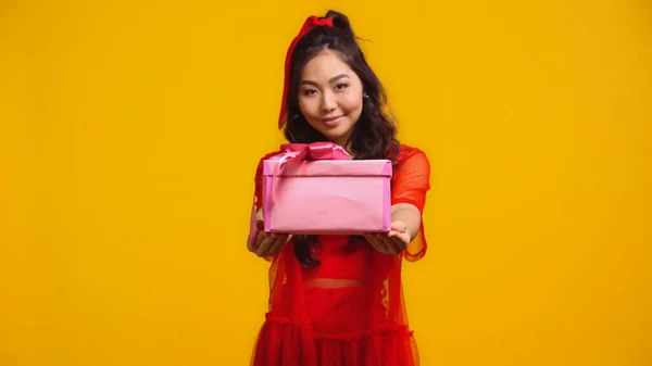 Joyful young asian woman holding wrapped present isolated on yellow — Stock Photo