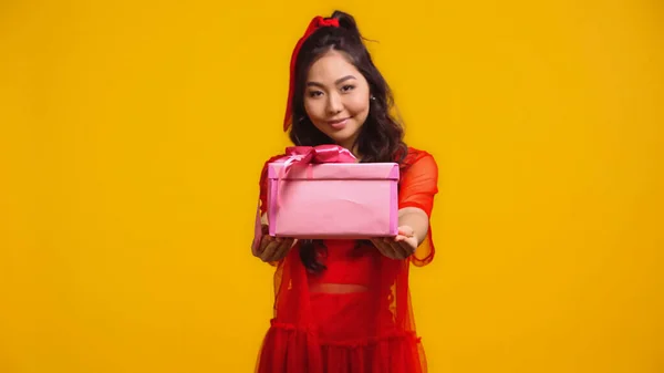 Joyeuse jeune asiatique femme tenue enveloppé présent isolé sur jaune — Photo de stock