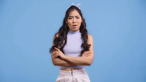 Dissatisfied asian woman in crop top standing with crossed arms isolated on blue — Stock Photo